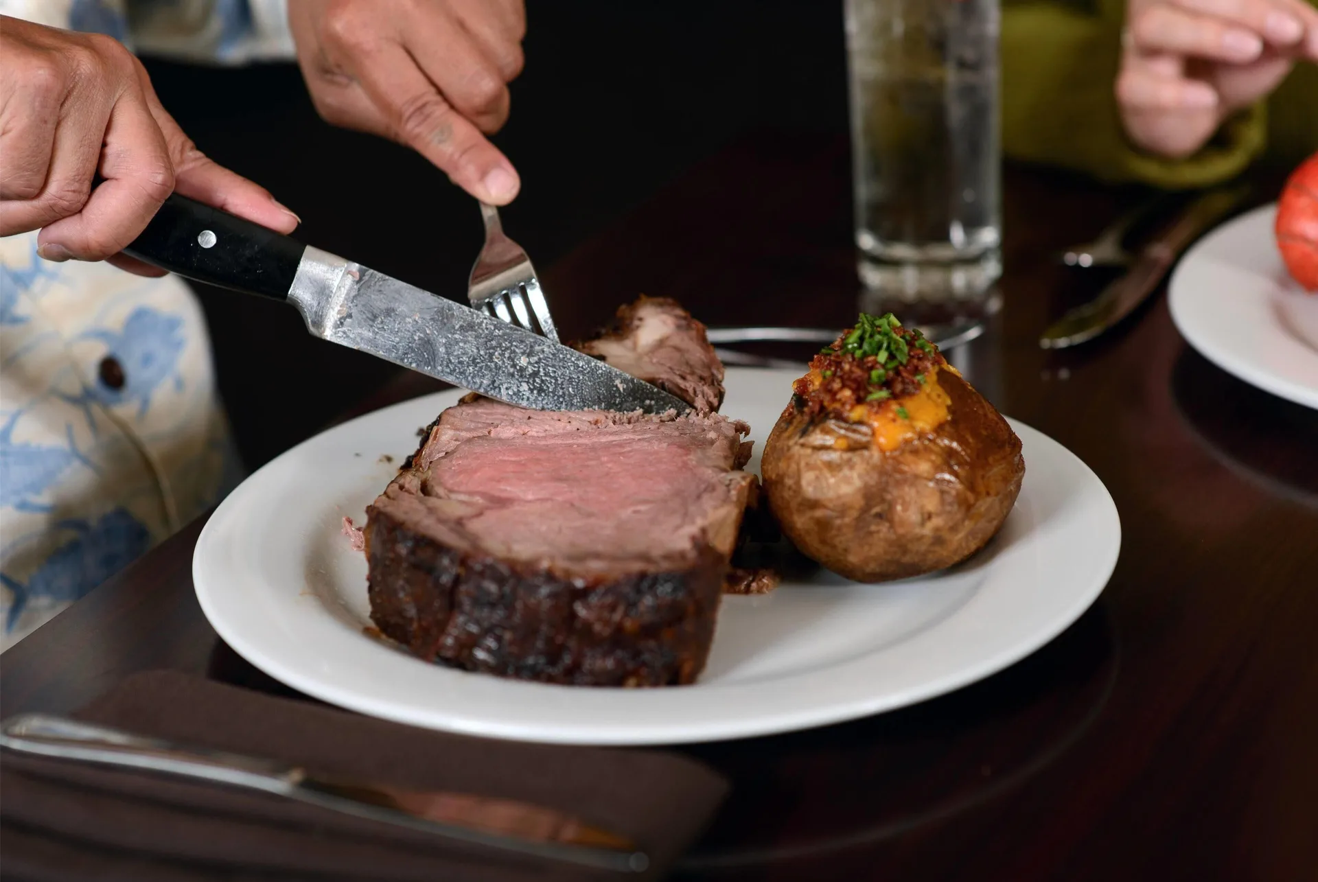 A steak dinner being cut beside a loaded baked potato at Hilo Hawaiian Hotel.