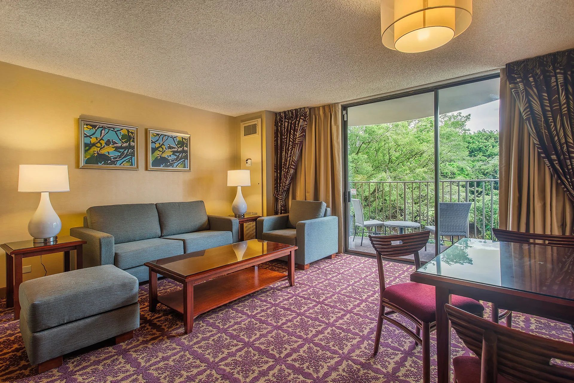 Suite living room with sofa, dining table, and balcony greenery at Hilo Hawaiian Hotel.