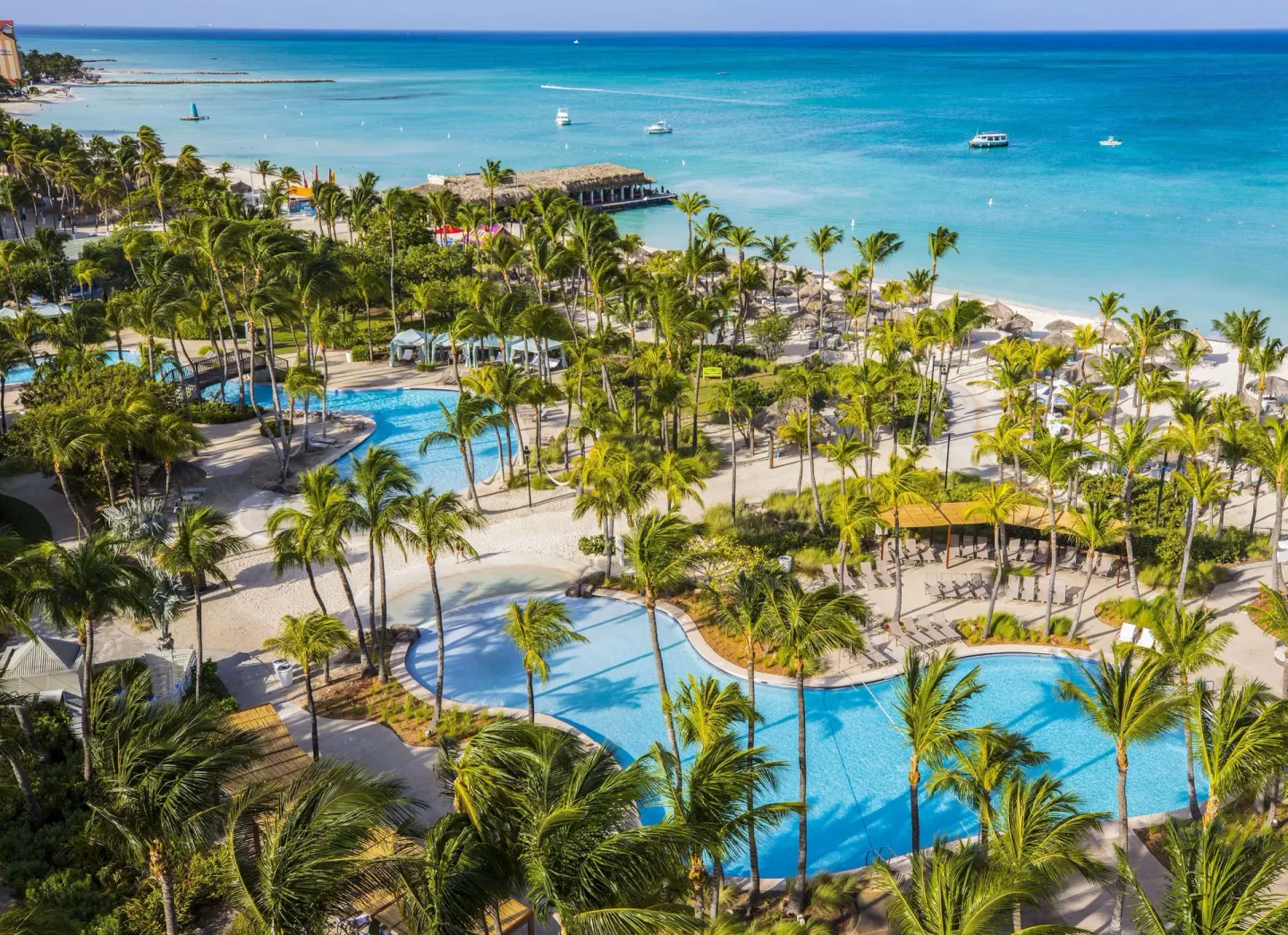 Aerial view of pools, palms, beach, and turquoise sea at Hilton Aruba Caribbean Resort and Casino.