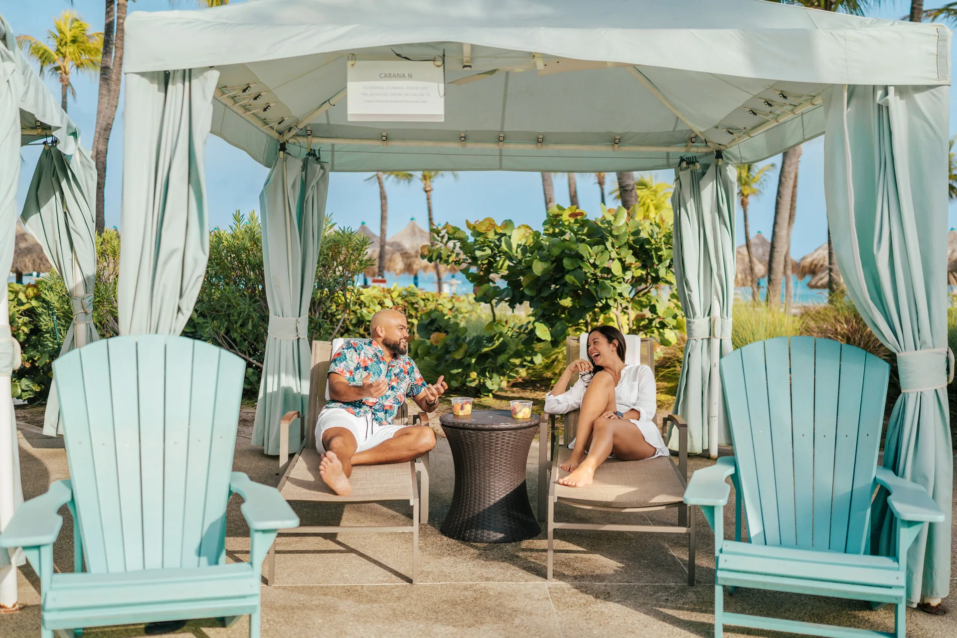Guests relax in a shaded beach cabana at Hilton Aruba Caribbean Resort and Casino.