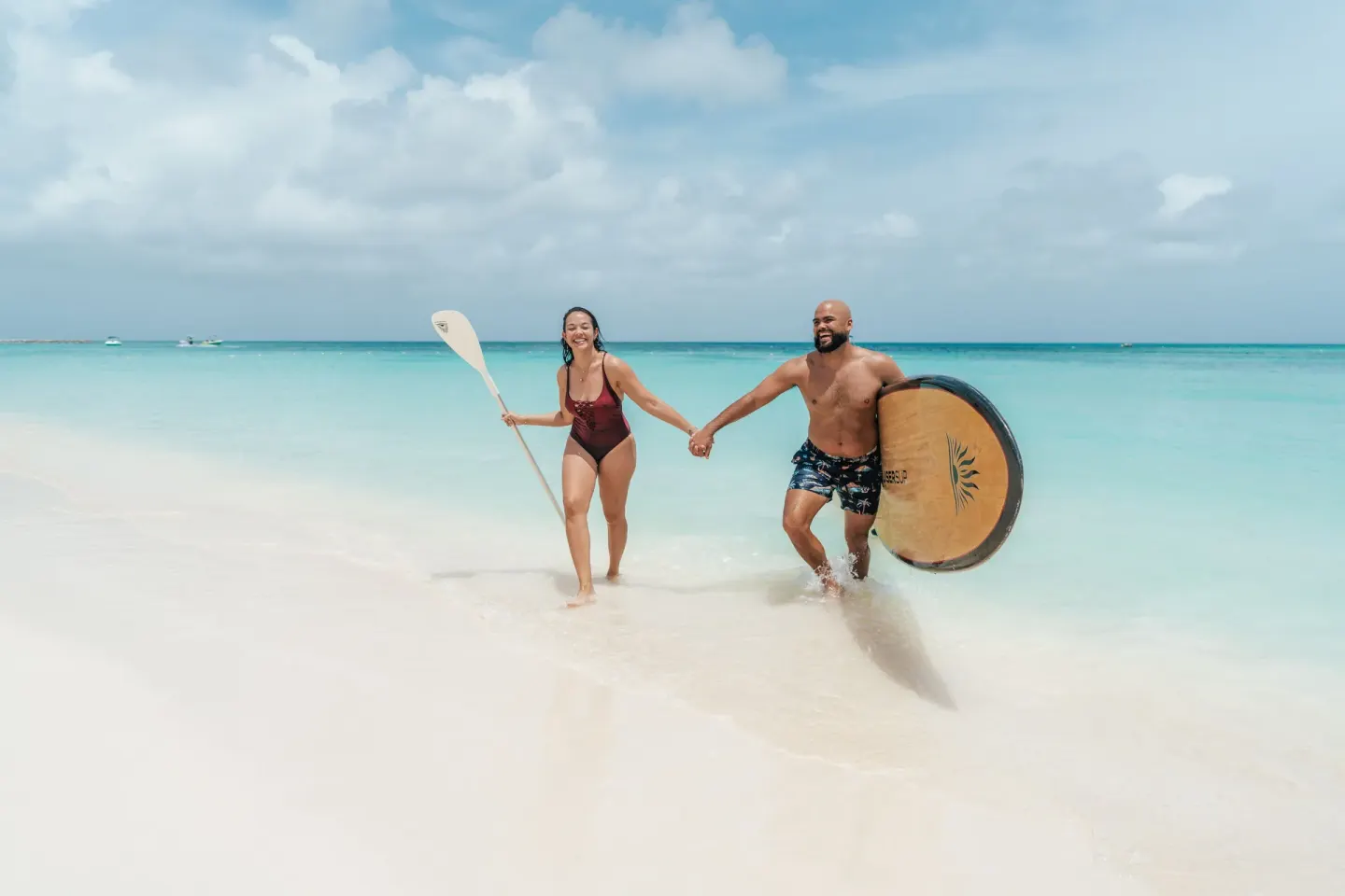 Two beachgoers carry paddleboards in the surf at Hilton Aruba Caribbean Resort and Casino.