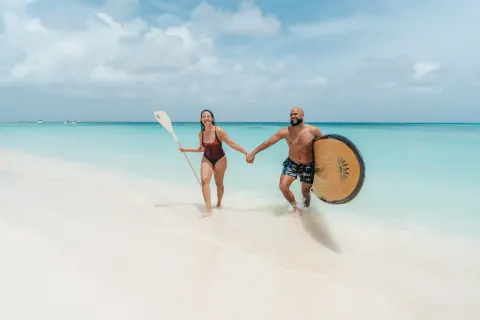 Two beachgoers carry paddleboards in the surf at Hilton Aruba Caribbean Resort and Casino.