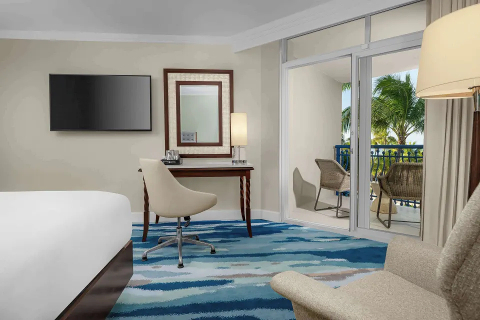 Partial ocean view room with bed, desk, TV, and balcony seating at Hilton Aruba Caribbean Resort and Casino.