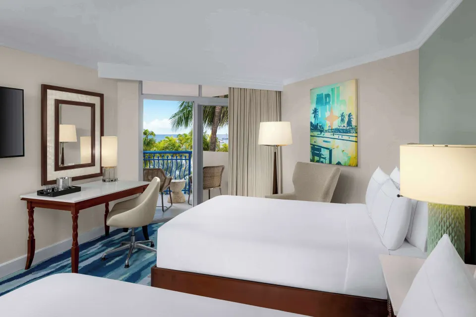 Partial ocean view room with two beds, desk, balcony, and palms at Hilton Aruba Caribbean Resort and Casino.