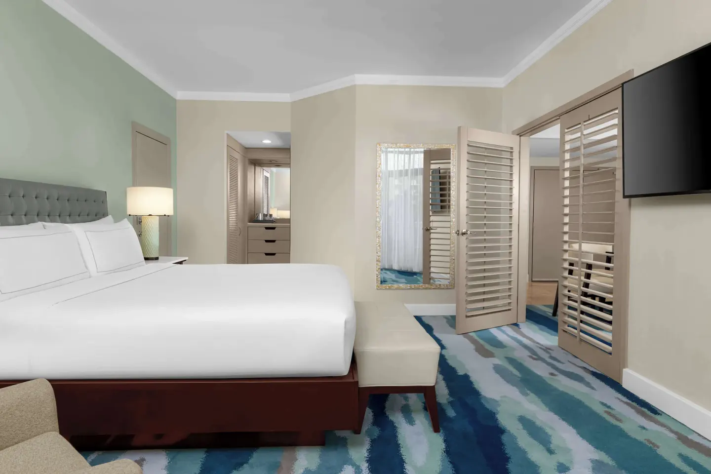 Suite bedroom with king bed, shutters, and wall TV at Hilton Aruba Caribbean Resort and Casino.