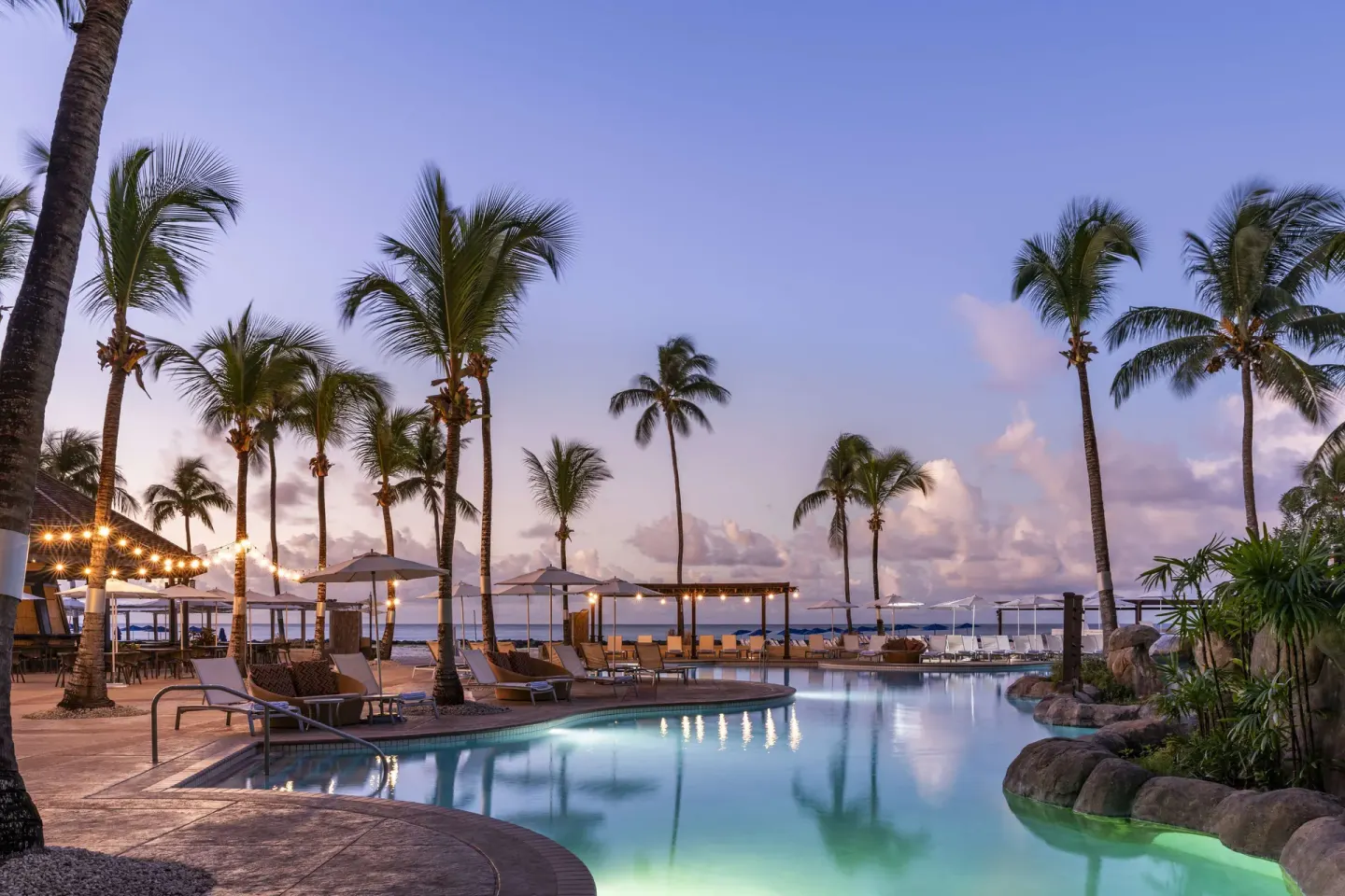 Evening pool scene with palms, loungers and ocean beyond at Hilton Barbados Resort.