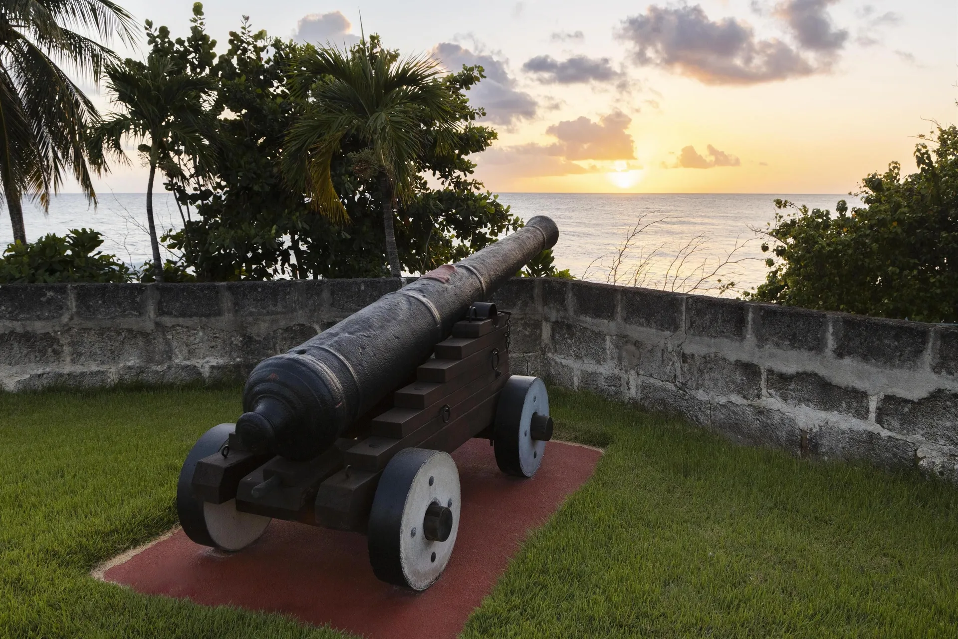 Historic cannon on a lawn faces the ocean at sunset at Hilton Barbados Resort.