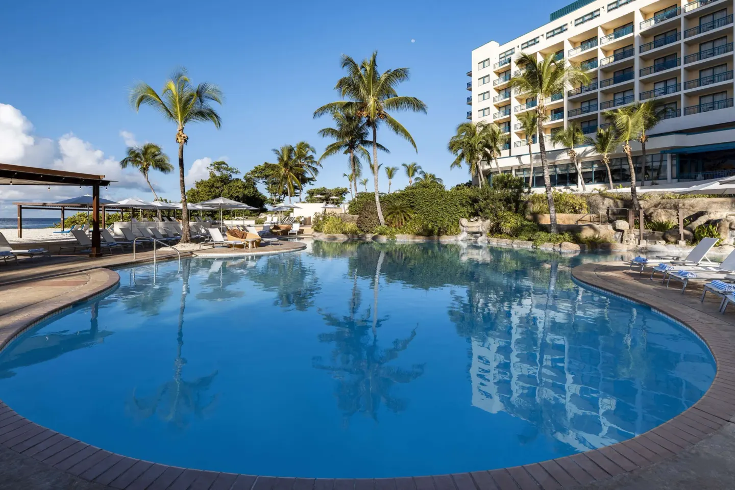 Lagoon-style pool with palms, loungers and hotel building at Hilton Barbados Resort.