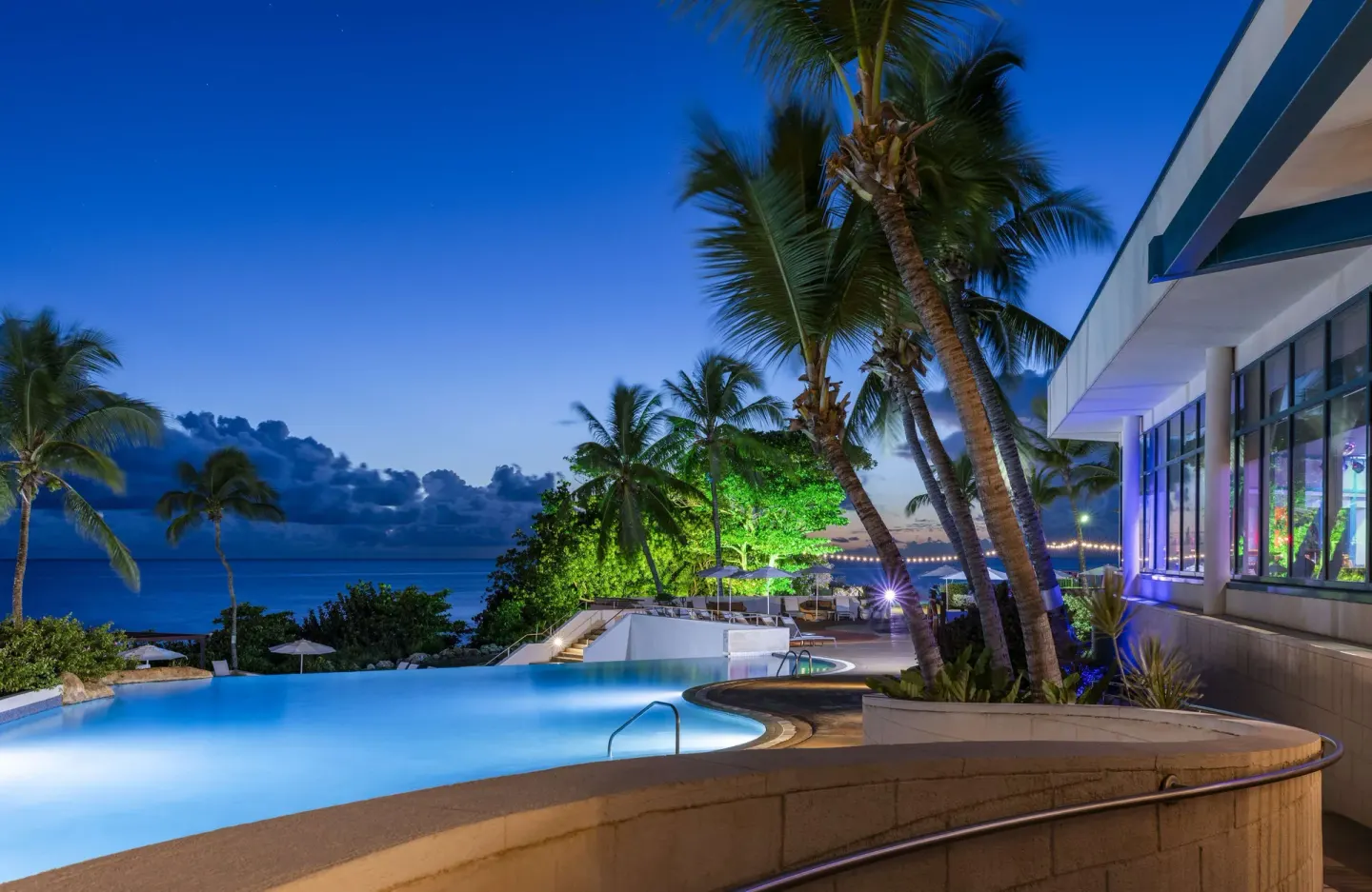 Pool terrace with palms and ocean at Hilton Barbados Resort at twilight.