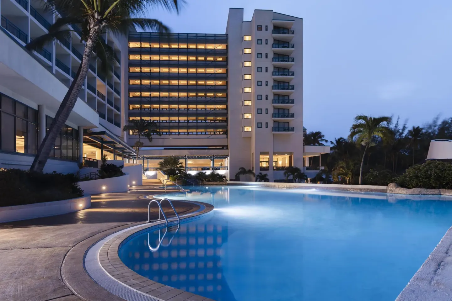 Illuminated resort pool and hotel towers at dusk at Hilton Barbados Resort.