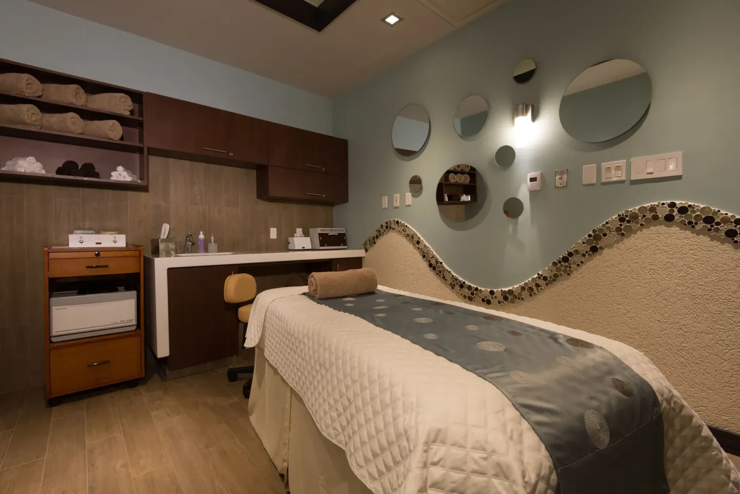 Single spa treatment bed with round mirrors and towel shelving at Hilton Barbados Resort.