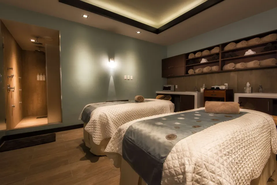 Two spa treatment beds with towels, sinks, and a shower area at Hilton Barbados Resort.