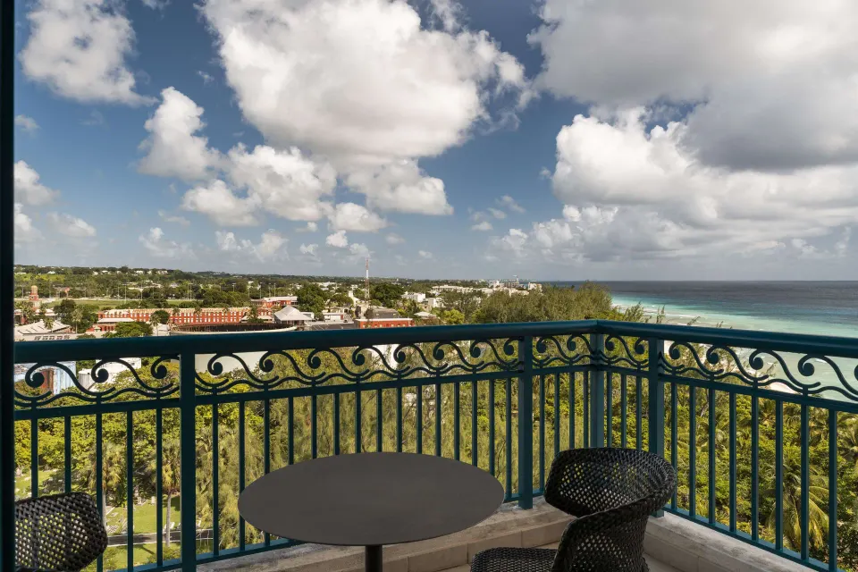 Corner room balcony with table, chairs, ocean, and island views at Hilton Barbados Resort.