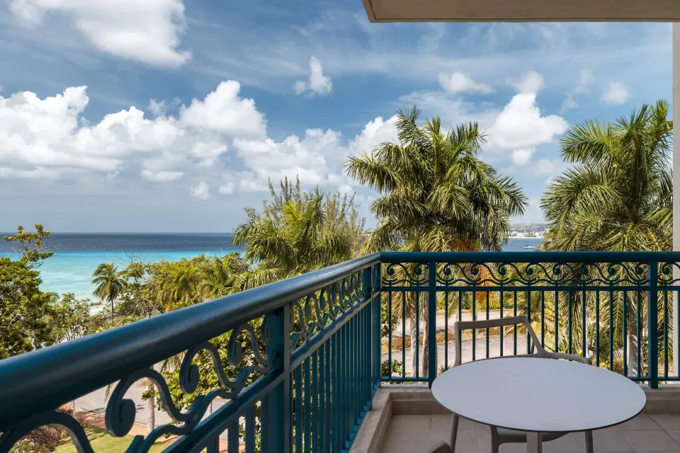 Corner room balcony with table, railing, palms, and ocean view at Hilton Barbados Resort.