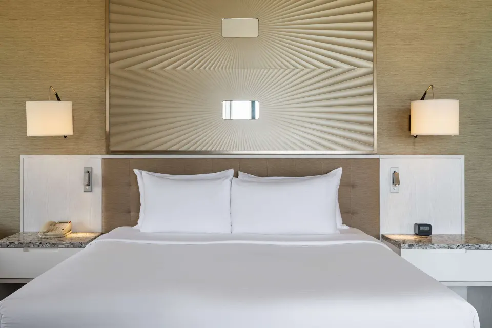 Corner room king bed with white bedding and wall sconces at Hilton Barbados Resort.