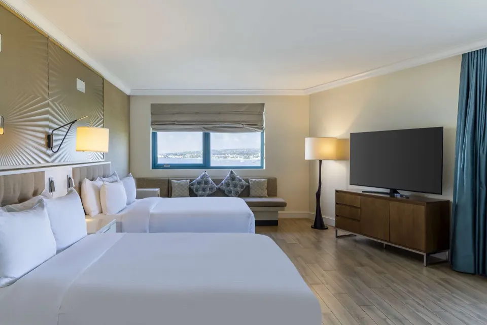 Corner room with two beds, seating, TV, and window view at Hilton Barbados Resort.