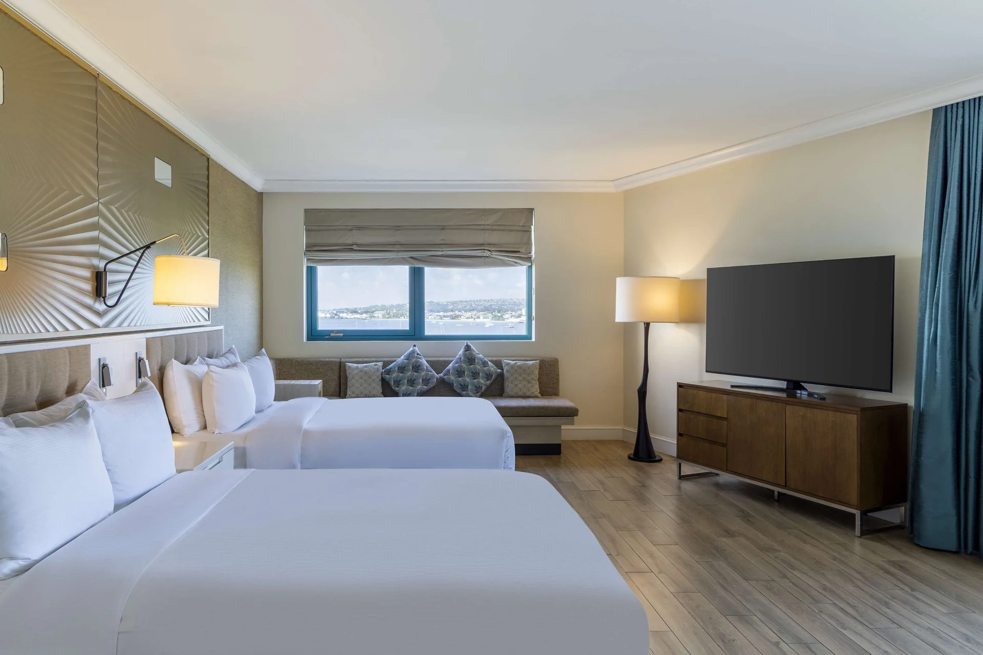 Corner room with two beds, seating, TV, and window view at Hilton Barbados Resort.