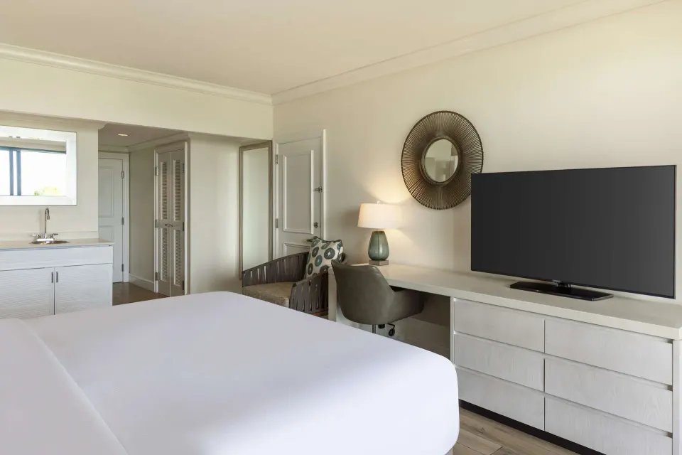 One Bedroom Suite king bed with desk, dresser and TV at Hilton Barbados Resort.