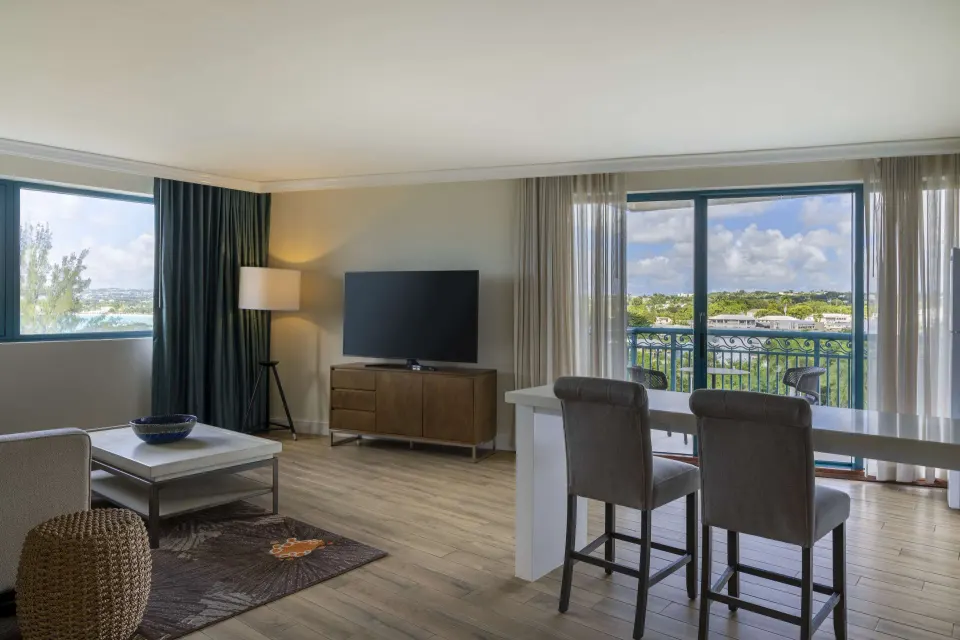 One Bedroom Suite living room with TV, dining counter and balcony at Hilton Barbados Resort.