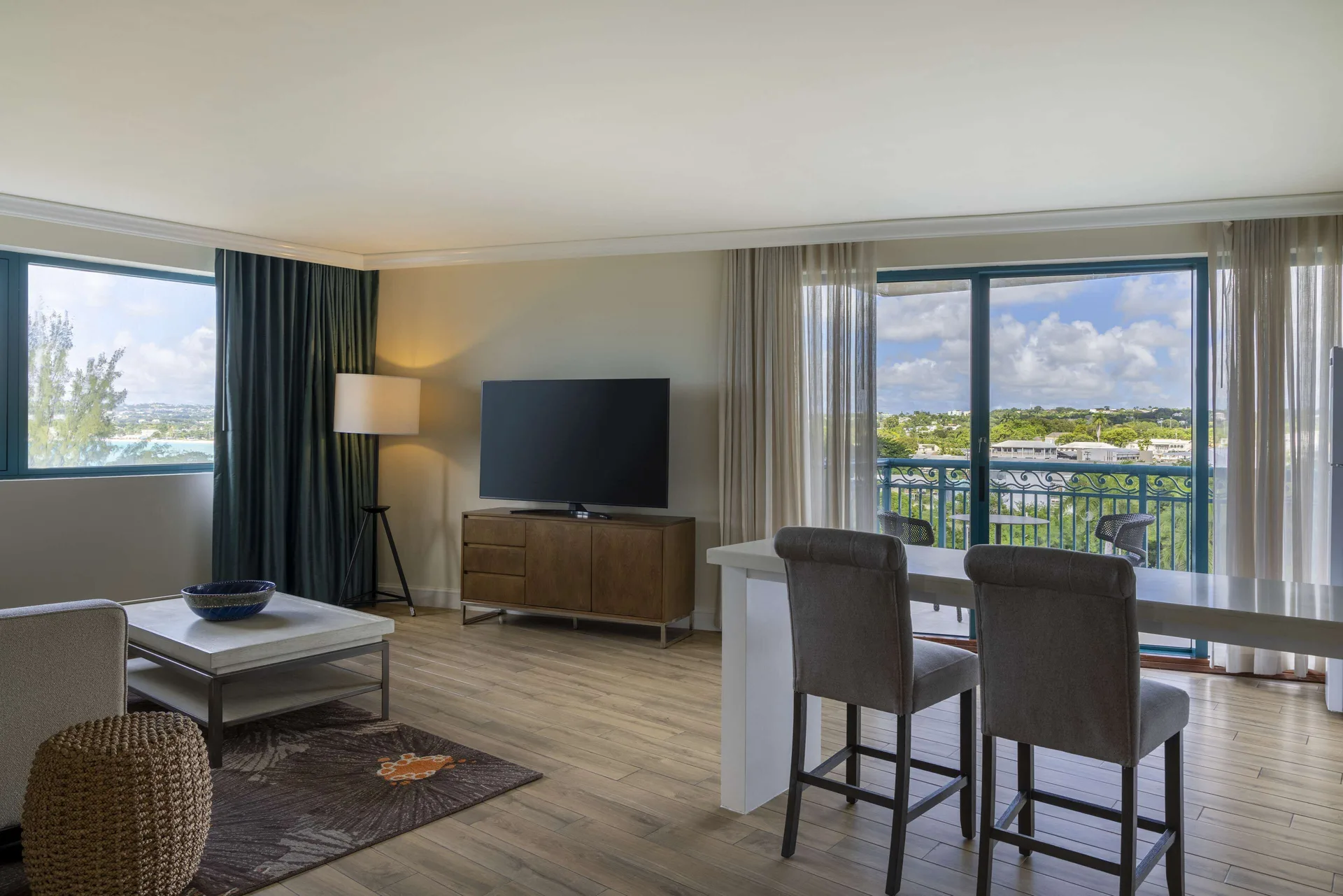 One Bedroom Suite living room with TV, dining counter and balcony at Hilton Barbados Resort.