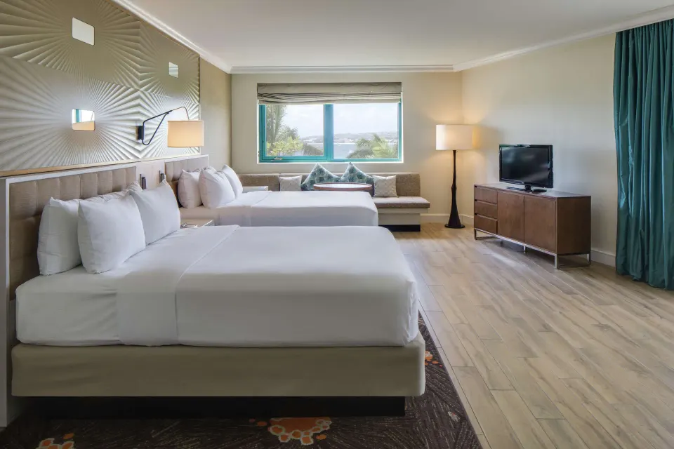 Corner ocean view suite bedroom with two beds and sitting area at Hilton Barbados Resort.