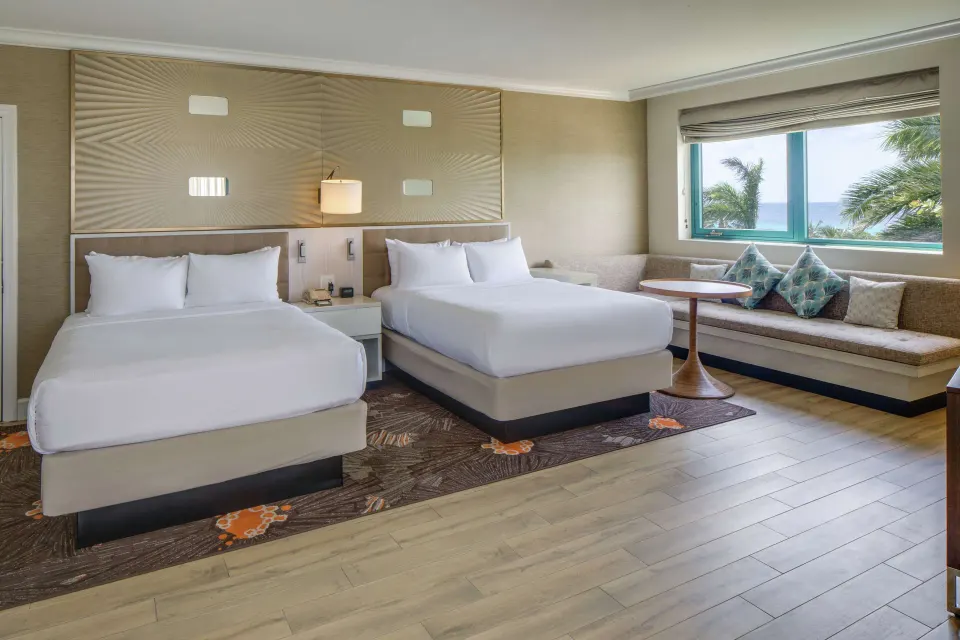 Corner ocean view suite with two beds and window bench at Hilton Barbados Resort.