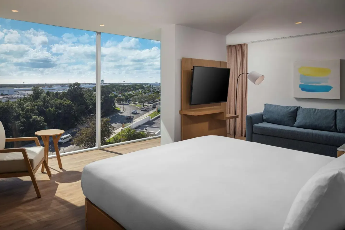 Corner king-bed guest room with sofa and large windows at Hilton Garden Inn Cancun Airport.