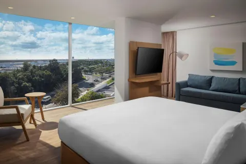 Corner king-bed guest room with sofa and large windows at Hilton Garden Inn Cancun Airport.