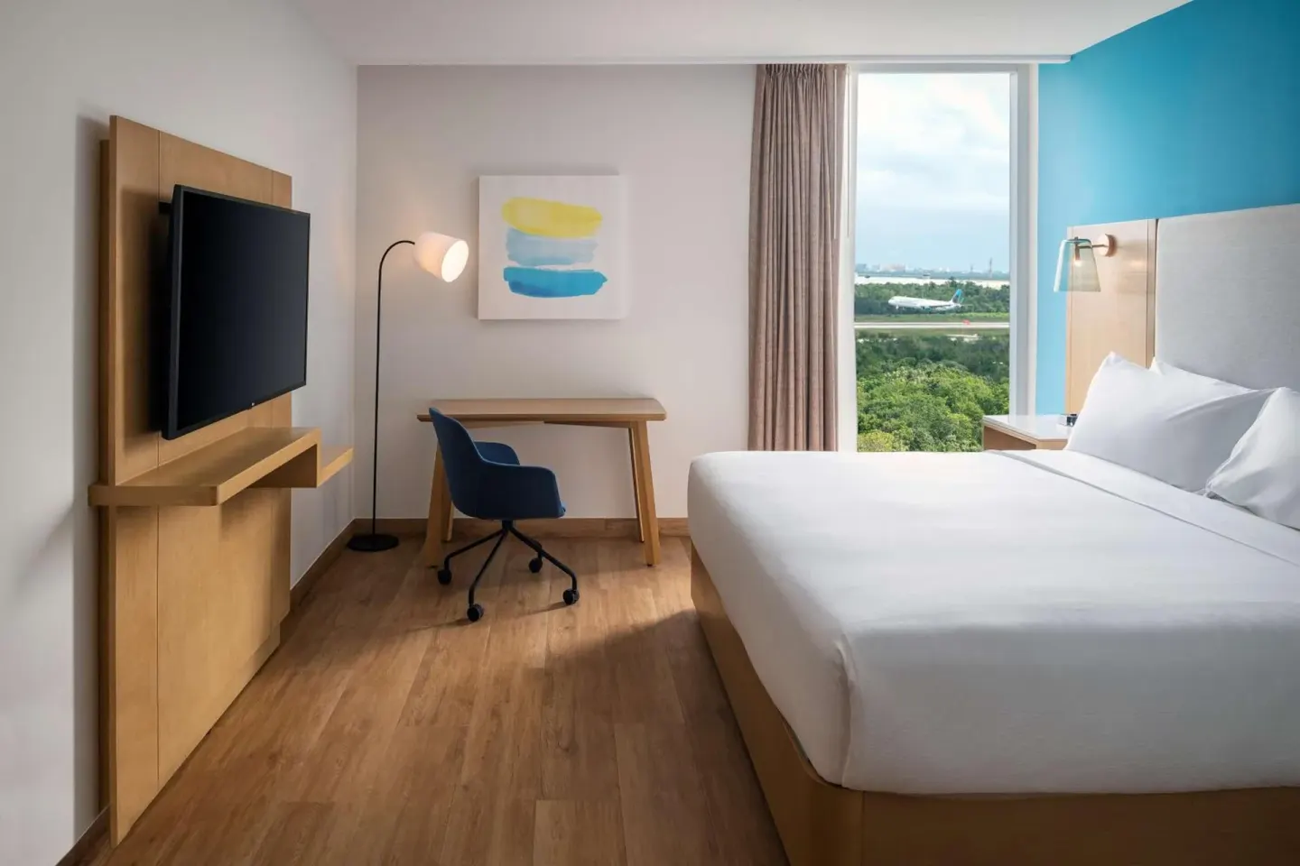 King guest room with desk, TV, and airport-facing window at Hilton Garden Inn Cancun Airport.