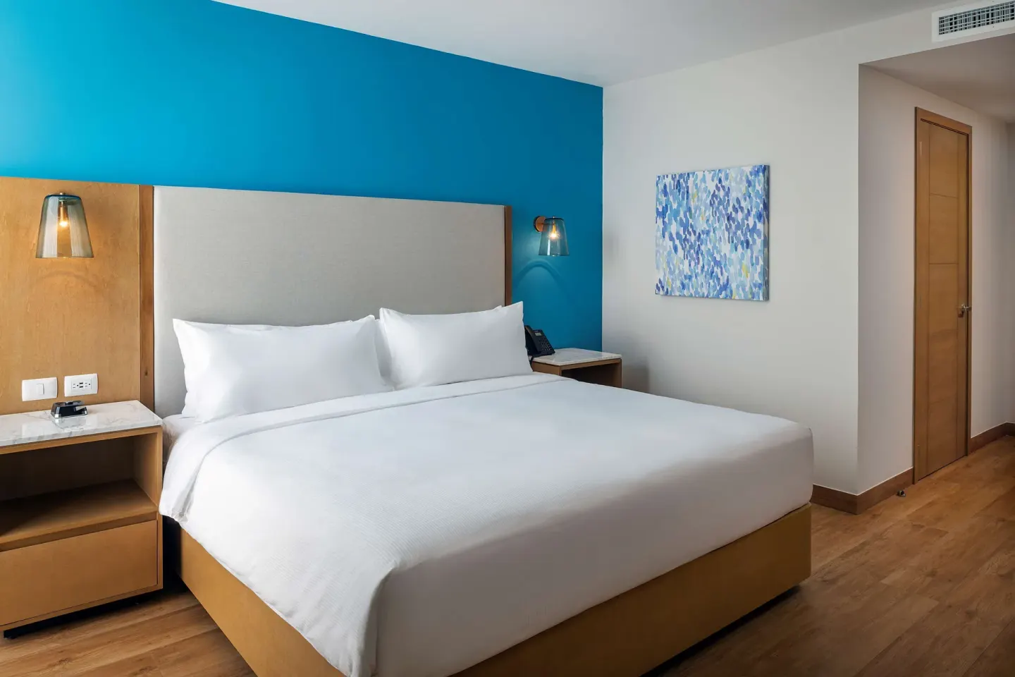 Accessible king room bed with blue accent wall at Hilton Garden Inn Cancun Airport.