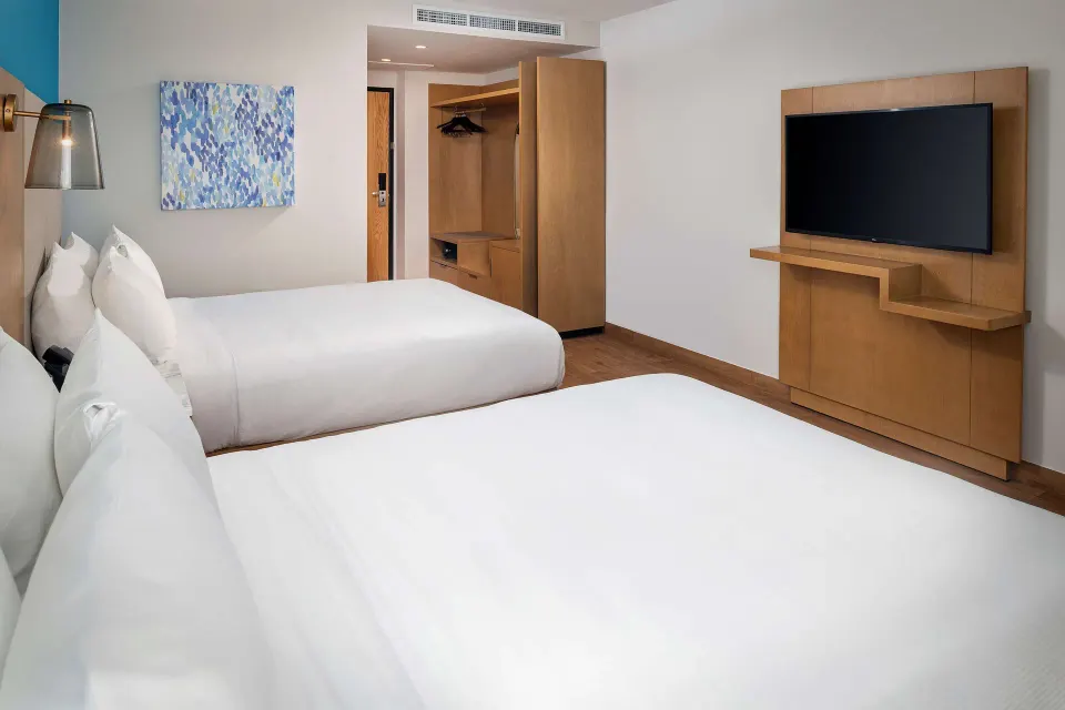 Two-bed guest room with TV and open closet at Hilton Garden Inn Cancun Airport.