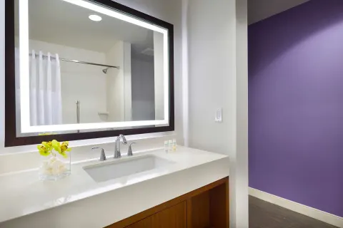 Cottage vanity with lighted mirror, sink, and purple accent wall at Hilton Garden Inn Kauai Wailua Bay.