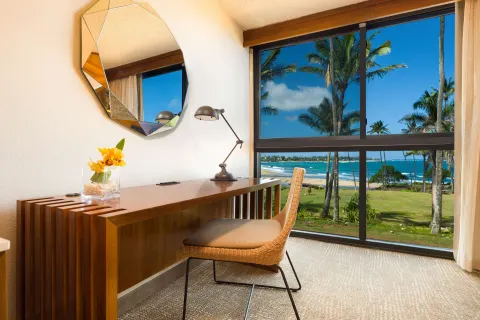 Ocean view room desk and window at Hilton Garden Inn Kauai Wailua Bay overlooking palms and beach.
