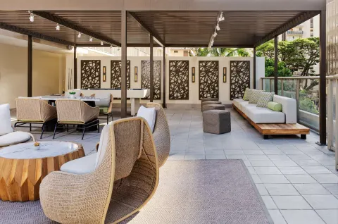 Covered terrace lounge with wicker chairs at Hilton Garden Inn Waikiki Beach.