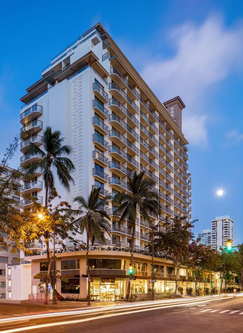 Hotel tower exterior at dusk with palm trees at Hilton Garden Inn Waikiki Beach.