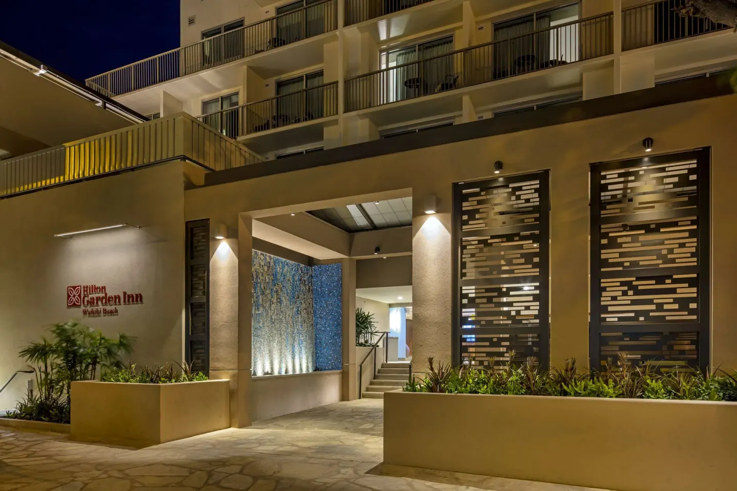 Nighttime hotel entrance with balconies and illuminated landscaping at Hilton Garden Inn Waikiki Beach.