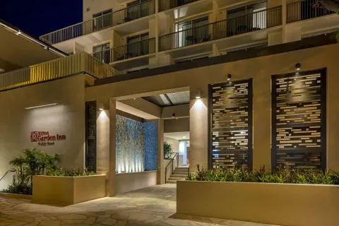 Nighttime hotel entrance with balconies and illuminated landscaping at Hilton Garden Inn Waikiki Beach.