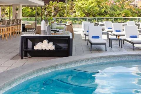 Pool edge with loungers, towels, and bar seating at Hilton Garden Inn Waikiki Beach.