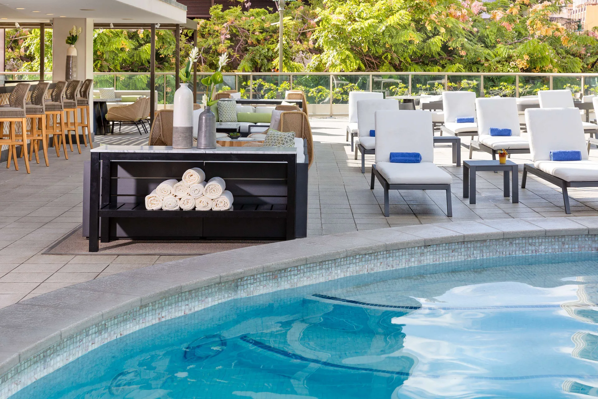 Pool edge with loungers, towels, and bar seating at Hilton Garden Inn Waikiki Beach.