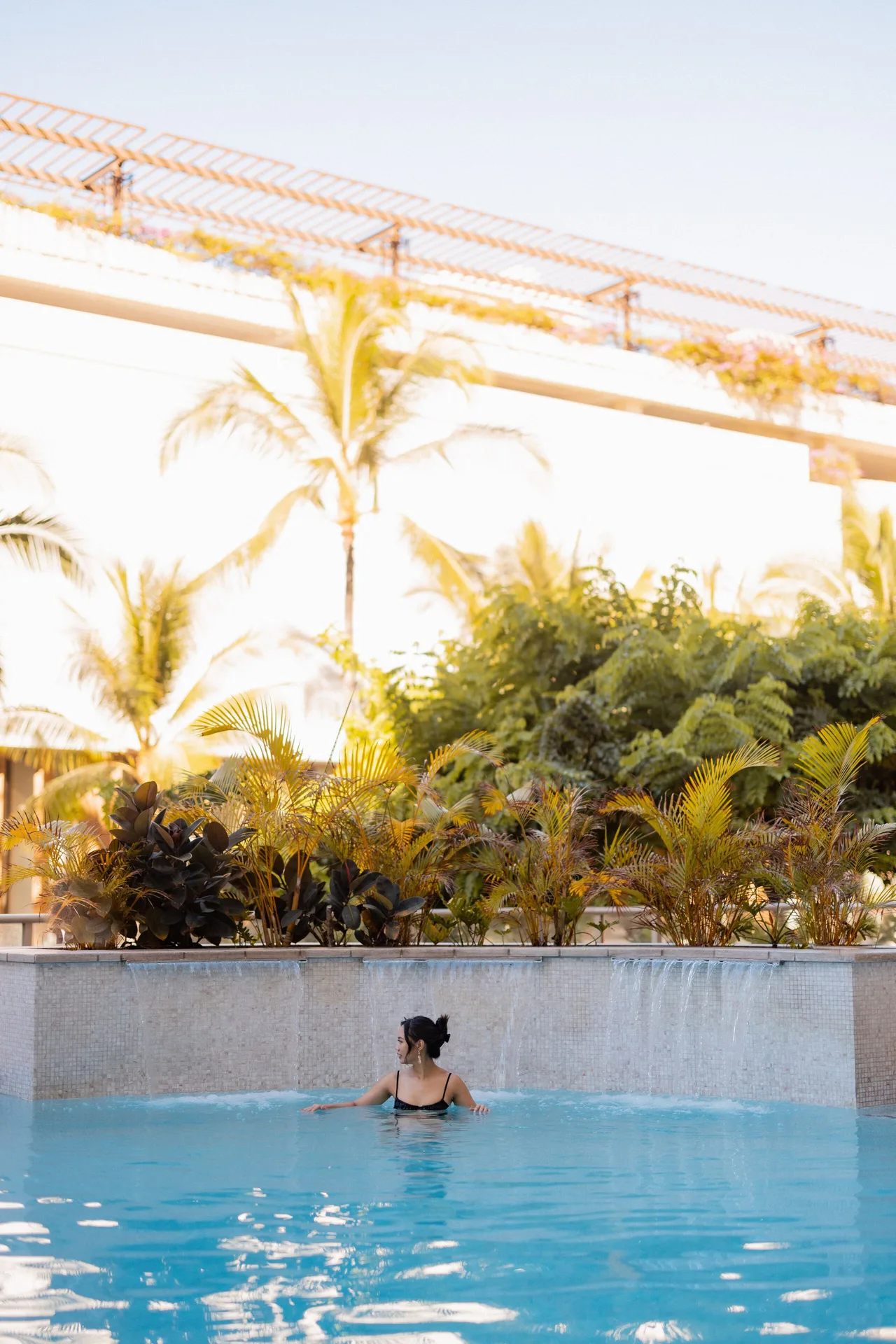 Guest swimming beside a waterfall edge at the pool at Hilton Garden Inn Waikiki Beach.