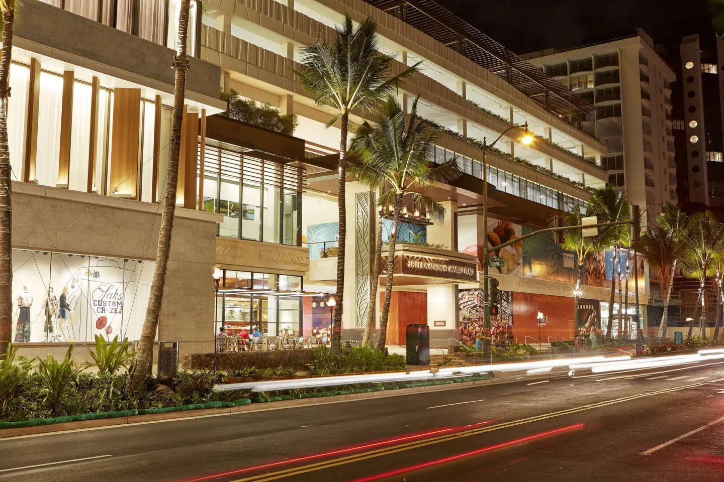 Street-level exterior with palm trees and light trails at Hilton Garden Inn Waikiki Beach.