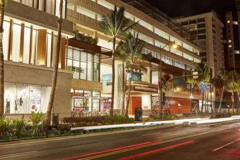 Street-level exterior with palm trees and light trails at Hilton Garden Inn Waikiki Beach.