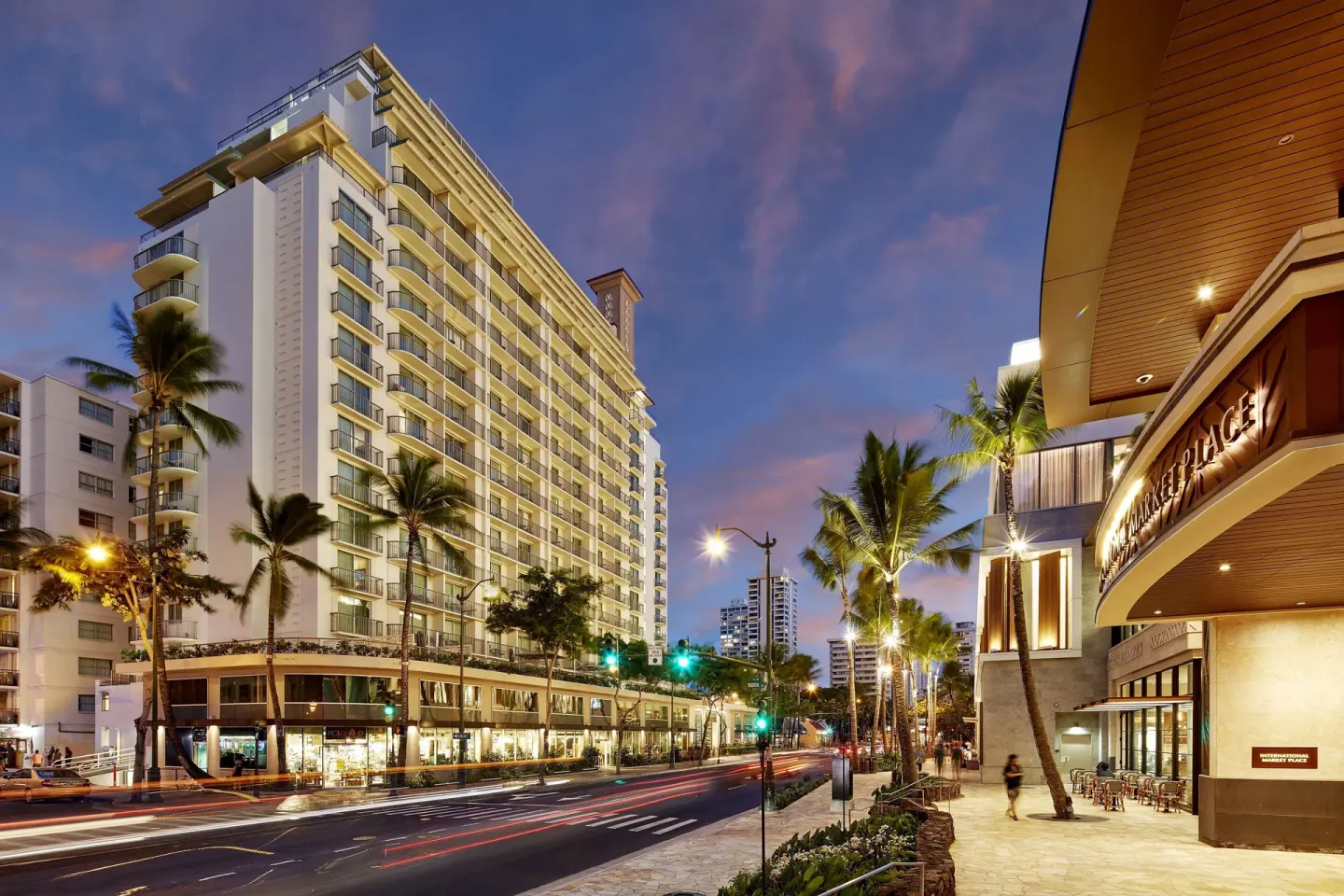 Twilight Waikiki street scene beside Hilton Garden Inn Waikiki Beach with palm trees and traffic lights.