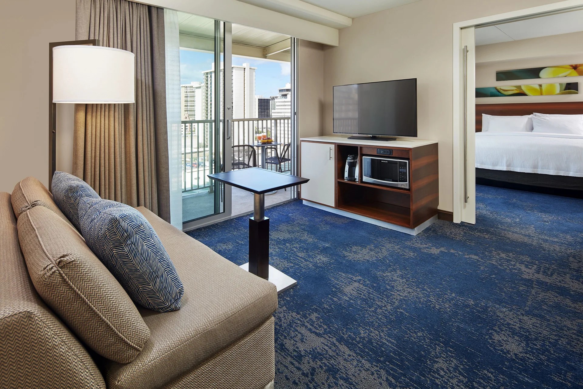 Suite living room with sofa and bedroom doorway at Hilton Garden Inn Waikiki Beach.