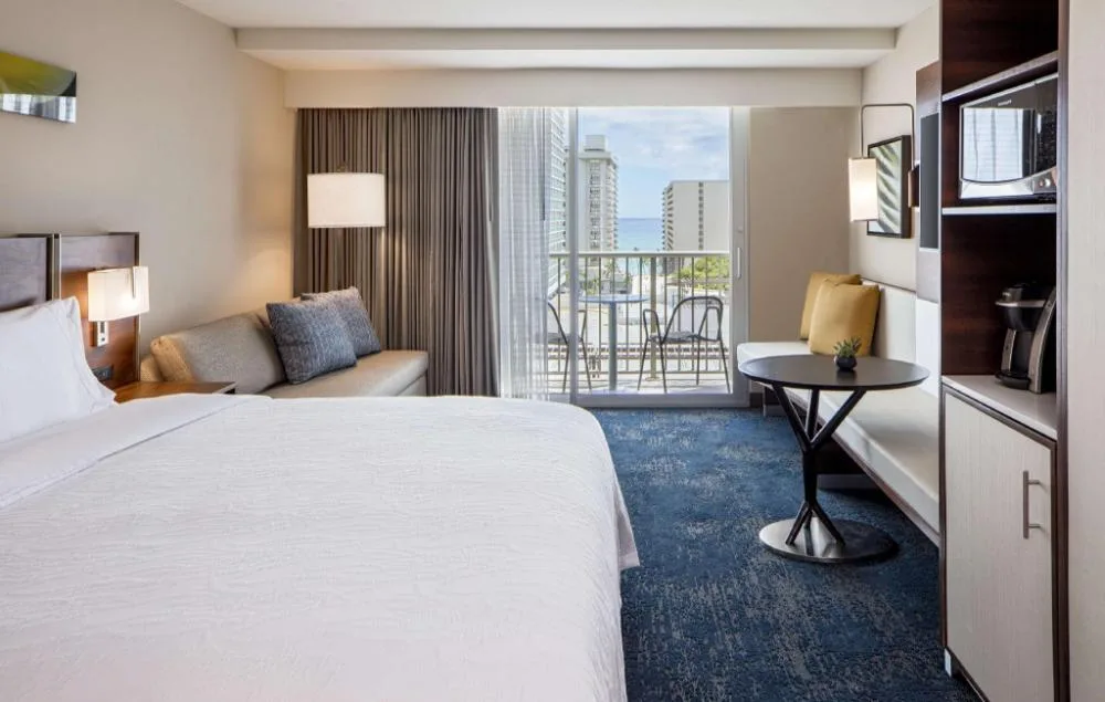 Partial ocean view room with sofa and balcony at Hilton Garden Inn Waikiki Beach.