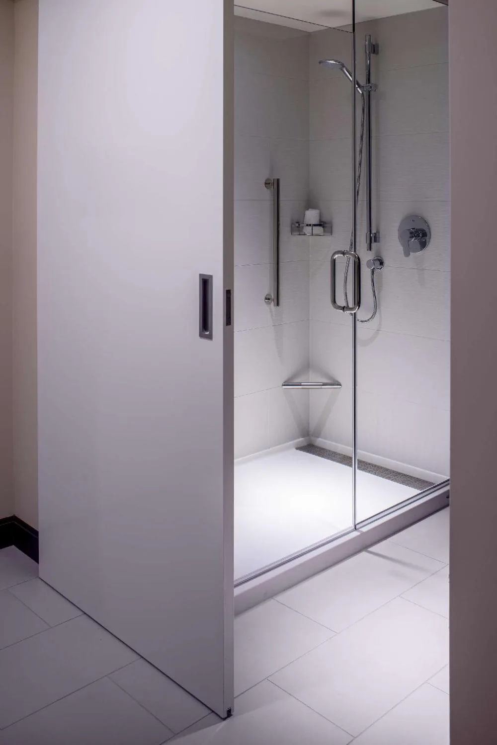 Accessible guest bathroom shower with glass door and grab bars at Hilton Garden Inn Waikiki Beach.