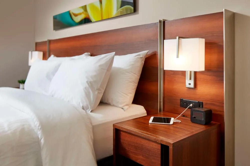 Suite bedroom with double bed, wood headboard and bedside charging at Hilton Garden Inn Waikiki Beach.