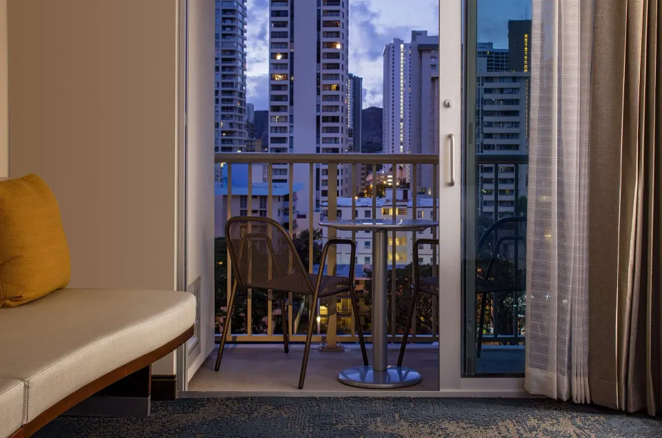 Accessible room balcony with seating and city buildings at Hilton Garden Inn Waikiki Beach.