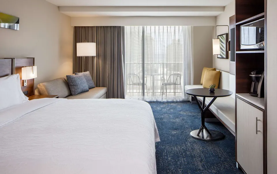 Standard Room with king bed, sofa bed, table, and sheer balcony curtains at Hilton Garden Inn Waikiki Beach.