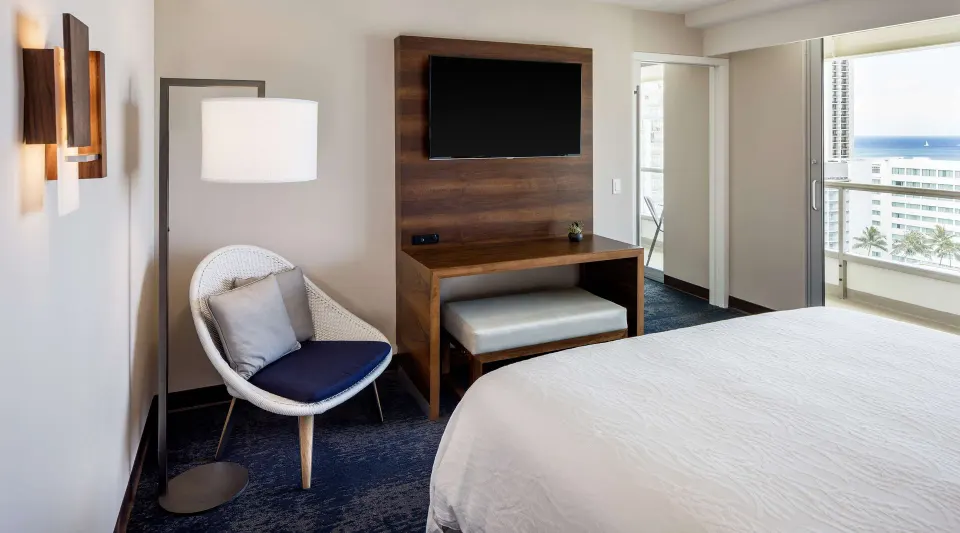 Accessible suite king bed area with chair, TV, bench, and balcony view at Hilton Garden Inn Waikiki Beach.
